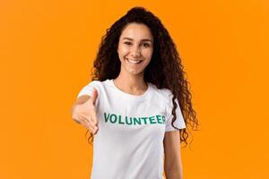 Cheerful Volunteer Woman Offering Hand For Handshake Greeting To Camera Posing Standing Over Yellow Studio Background. Volunteering, Voluntary Work, Join Our Team Concept photo