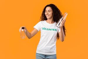 No More Plastic. Female Volunteer Choosing Between Glass And Plastic Bottle Posing Standing In Studio Over Yellow Background. Stop Using Single-Used Bottles, Ecology Concept photo