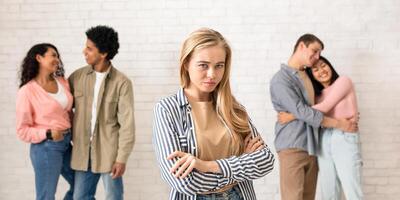 Relationships, love and loneliness. Sad young blonde student and two multiracial couples hugging in college or university, on white brick wall background, panorama, copy space, studio shot photo