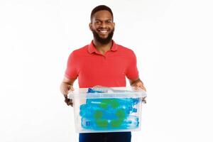 Black Guy Holding Box With Recycle Symbol Full Of Used Plastic Bottles Sorting His Waste For Disposal Standing On White Studio Background, Smiling To Camera. Junk Sorting And Recycling Concept photo