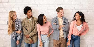 Interesting offer and team, education and study with group in college or university. Smiling teens multiracial people look at spanish female friend, on white wall background, studio shot, empty space photo