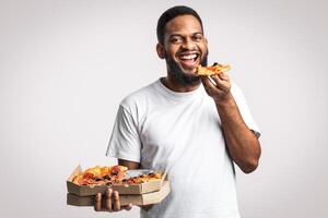 Happy Black Guy Enjoying Pizza Posing With Pizzeria Box Enjoying Junk Food Standing Smiling To Camera Over White Background, Studio Shot. Pizza Restaurant Delivery Advertisement, Cheat Meal Concept photo