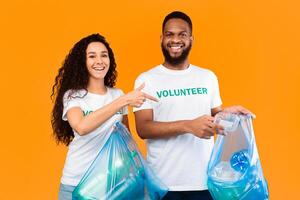 Don't Litter. Male And Female Multicultural Volunteers Picking Wasted Plastic Cleaning And Sorting Trash Holding Blue Garbage Bags Posing Over Yellow Studio Background. Ecology, Keep Environment Clean photo