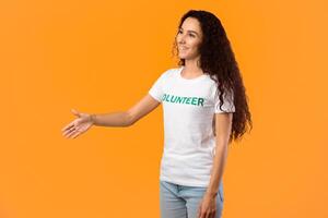 Side View Of Volunteer Lady Stretching Hand For Handshake Greeting Aside Posing Standing Over Yellow Studio Background. Join Our Team, Volunteering, Voluntary Work Concept photo