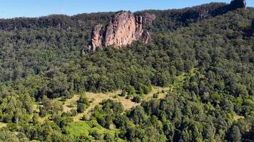Aerial footage captures the iconic Nimbin Rocks surrounded by dense forest under bright daylight, showcasing natural beauty and geological formations video