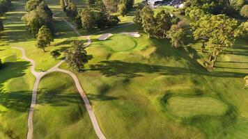 Drone footage captures a serene golf course landscape with vibrant greens and long shadows during sunset video