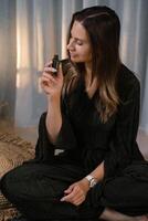 Woman holding essential oil bottle while sitting calmly on the floor in a serene indoor environment during a relaxing moment of self-care and mindfulness practice at dusk photo