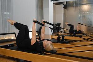 Woman practicing Pilates on reformer equipment in a bright studio with mirrors during a morning session focused on strength and flexibility exercises photo