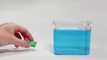 Hands manipulate a green clay ball, testing its buoyancy in a clear container of blue water video
