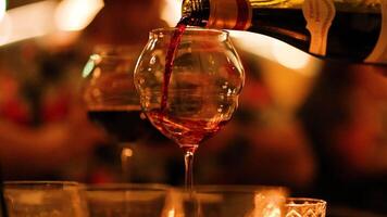 A bottle of red wine is poured into a glass in a warm, intimate setting with soft lighting video