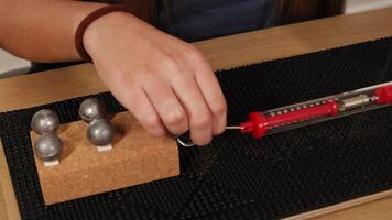 A hand uses a spring scale to measure the force needed to drag weights on a textured surface video