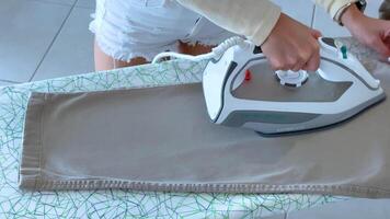 A person irons pants on a patterned board in bright lighting, showcasing domestic chores in a modern setting video