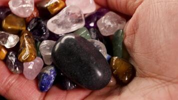A hand holds various chakra stones, including tiger's eye and amethyst, under soft lighting, highlighting their vibrant colors and textures video