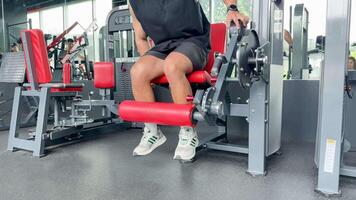 A person performs leg extensions on a machine in a well-lit gym environment, focusing on strength training video