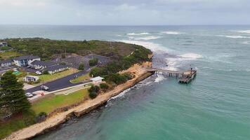 Drone captures sweeping views of Port Campbell's rugged coastline, pier, and lush greenery under overcast skies video