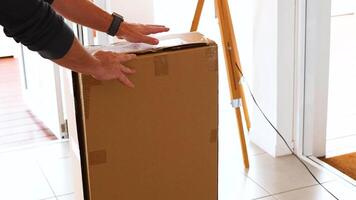 Hands carefully open a large cardboard box in a bright, sunlit room. Natural lighting and minimalistic decor create a calm atmosphere video