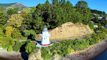 Aerial footage of Akaroa Lighthouse surrounded by lush greenery and turquoise waters under clear skies video