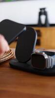 A hand places a smartphone on a sleek wireless charging dock beside a smartwatch in a modern, well-lit room video