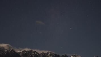 Time-lapse of clouds moving over starry sky and mountains in Queenstown, New Zealand. Captures serene nighttime atmosphere video