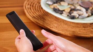 Hands replace batteries in a remote control on a wooden table with natural lighting and a decorative background video