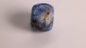 A Lapis Lazuli stone rotates on a white surface, highlighting its blue and gold hues under soft lighting video