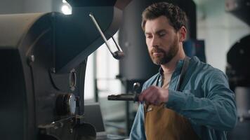 Caucasian man barista small business owner in factory coffee roaster machine working smelling fresh aroma roasted beans control roasting technology process caffeine smell fragrance enjoy smiling guy video