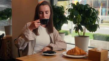 Caucasian woman drinking tasty good coffee in cafe girl female cafeteria visitor drink tea showing thumb up like gesture recommend restaurant food nutrition with croissant at table smiling at camera video