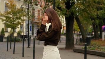 Back view Caucasian happy smiling walking in city girl woman enjoying sunny weather put on sunglasses turning around spinning on street lamppost having fun fooling stylish businesswoman female walk video