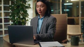 Busy stressed multitasking Asian Korean business woman working laptop businesswoman female talking mobile phone cellphone call with client checking papers read documents girl office employee overwork video