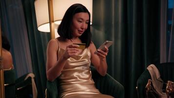Happy smiling Asian woman shopping online with credit card payment with mobile phone Korean female Japanese Chinese lady indoors buying online with smartphone successful transaction e-commerce app video