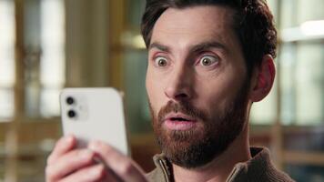 Shocked business man close up scared big eyes guy looking at mobile phone amazing shock news businessman at office frightened Caucasian male afraid stunned astonishment emotion unbelievable excitement video