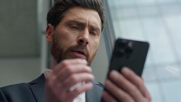 Close up Caucasian businessman business man in office worried anxiety sad thinking pensive about problem with mobile phone message bad news male employer entrepreneur with smartphone looking in window video