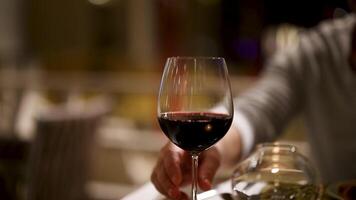 A person elegantly pours red wine into a glass at a dimly lit restaurant, creating a sophisticated and intimate atmosphere video