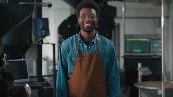 Confident happy African American man worker in coffee roasting fabric roasted cocoa technician smiling at camera posing male guy wearing apron working in coffeehouse distribution organic production video