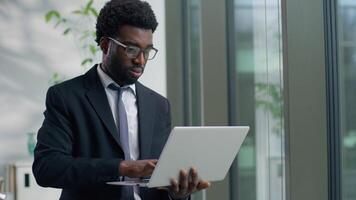 Close up African American pensive worry business man in office using laptop chatting typing online work trouble think solution difficult job task ethnic male businessman guy worker looking out window video