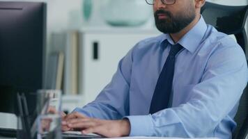 Concentrated Arabian businessman Muslim business man Indian male entrepreneur typing working online with computer looking at camera smiling guy at table CEO job occupation ambition marketing startup video