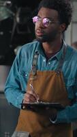 Confident smiling African American man worker in coffee roasting fabric work with roasted cocoa machine checking inspecting writing notes expertise quality control engineer professional guy working video