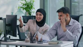 Two muslim business team in office working Islamic group Indian co-workers Arabian colleagues celebrate winning high five victory achievement work with computer online startup success corporate growth video