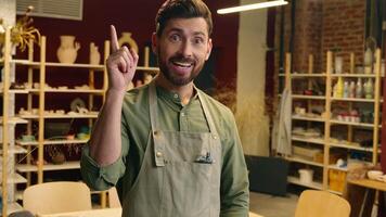 Happy creative smiling Caucasian guy man small business owner businessman potter craftsman crock male looking at camera thinking solution having brilliant idea eureka insight indoors workshop pottery video