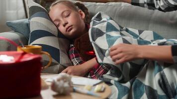 Caucasian family at home medicine health problem concept sleeping child kid sick ill daughter napping on couch caring mother covering with blanket little girl touch forehead checking temperature fever video