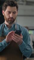 Caucasian man worker with smartphone in coffee roasted fabric industry working stand near roasting machine using mobile phone male small business owner inspecting quality browsing cellphone chatting video
