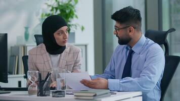 Two muslim business team in office working Islamic group Indian co-workers Arabian colleagues discuss paperwork papers document company rules work boss man talking helping consulting woman intern video