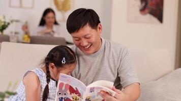 Father and daughter share a joyful reading moment on a sofa, with warm lighting and a relaxed atmosphere video