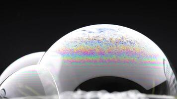 A soap bubble displays vibrant colors before bursting against a dark background, captured in detailed slow motion video
