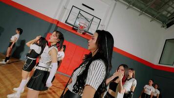 A group of dancers in a gymnasium, wearing striped outfits and performing a synchronized routine. The background features a basketball hoop and a vibrant sports environment. video