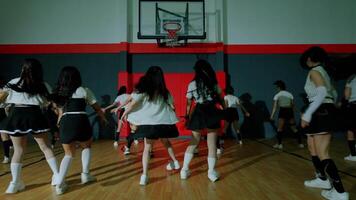 A group of dancers performing in a gymnasium, showcasing synchronized movements. They wear stylish outfits with a mix of black and white, emphasizing a dynamic and energetic atmosphere. video