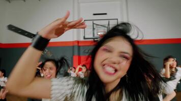 A dynamic dance performance in a gymnasium, featuring a group of energetic dancers in stylish outfits. The focus is on a central dancer with flowing hair, showcasing enthusiasm and movement. video