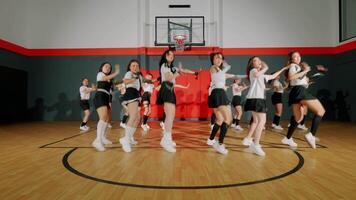 A dynamic dance performance in a gymnasium, featuring a group of dancers in coordinated outfits. They are showcasing energetic movements, with a basketball hoop in the background. video