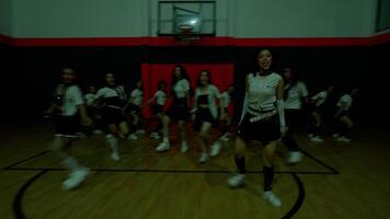 A group of dancers performing in a gymnasium, wearing stylish outfits. The scene captures dynamic movement and energy, with a basketball hoop in the background. video