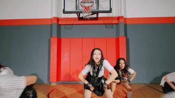A dancer performing in a gymnasium, wearing a stylish outfit with a striped top and a skirt. The background features a basketball hoop and red walls, creating a vibrant atmosphere. video